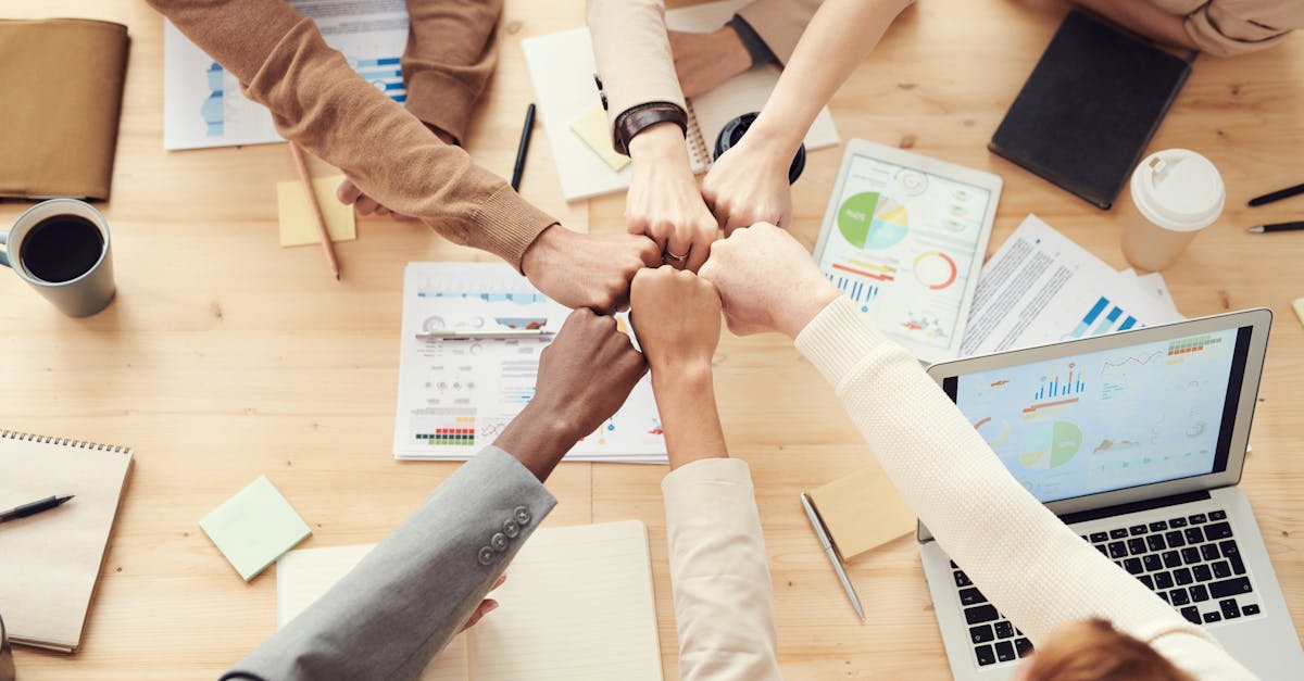 Top view of a diverse team fist bumping over a meeting table with paperwork and laptops, symbolizing teamwork.